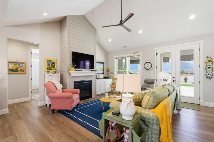 Living area with french doors, a high ceiling, ceiling fan, wood finished floors, and a large fireplace