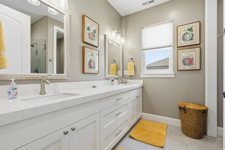 Full bathroom featuring double vanity, light tile patterned floors, and tiled shower