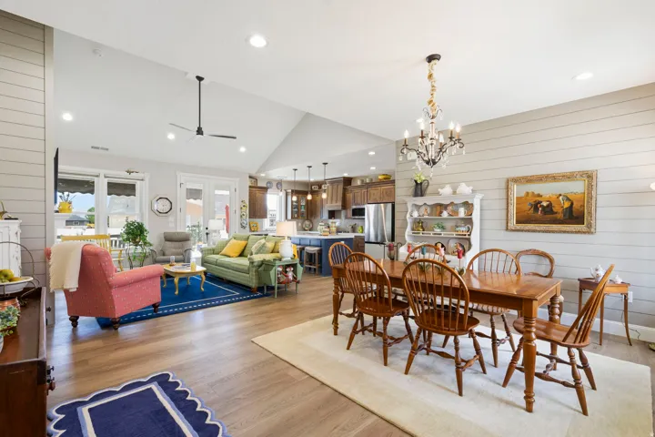Dining space with wooden walls, light wood-style flooring, ceiling fan, hanging lights, and vaulted ceiling