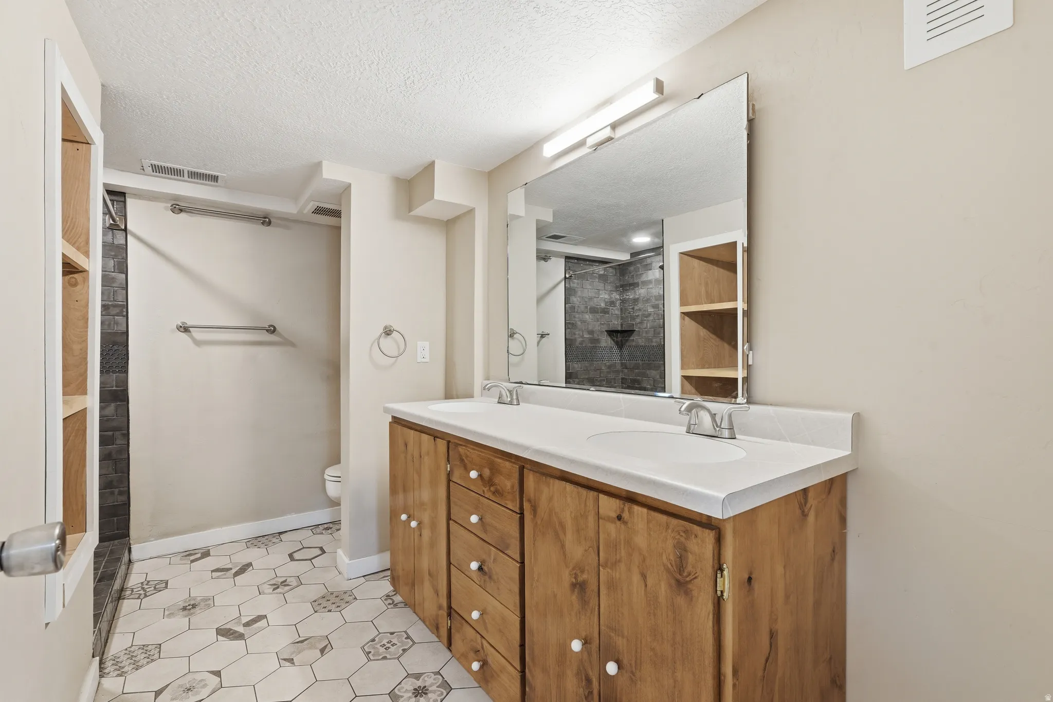 Full bathroom with double vanity, light tile patterned floors, and a textured ceiling
