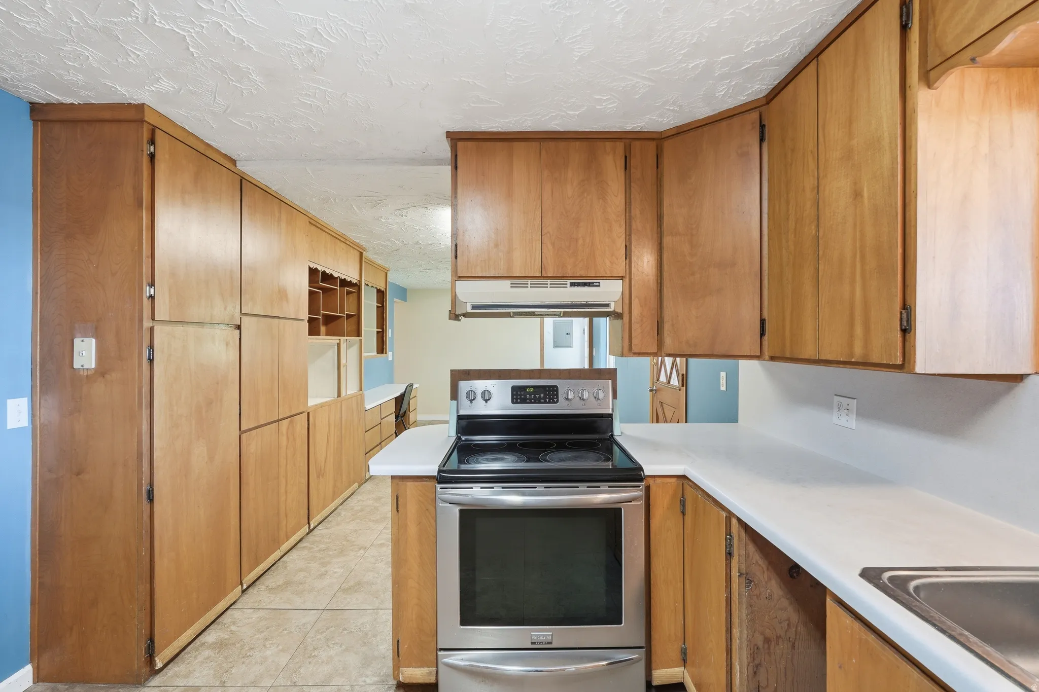 Kitchen featuring electric range, light countertops, a textured ceiling, wood finish cabinetry, and light tile patterned flooring