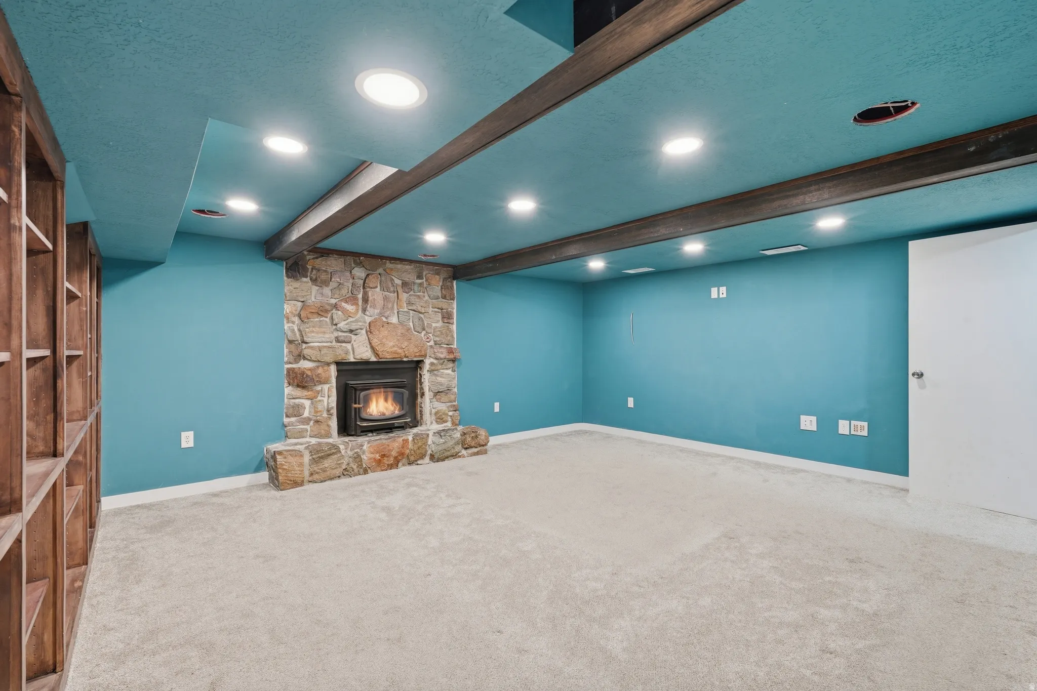 Unfurnished living room with carpet, beamed ceiling, a stone fireplace, a textured ceiling, and recessed lighting