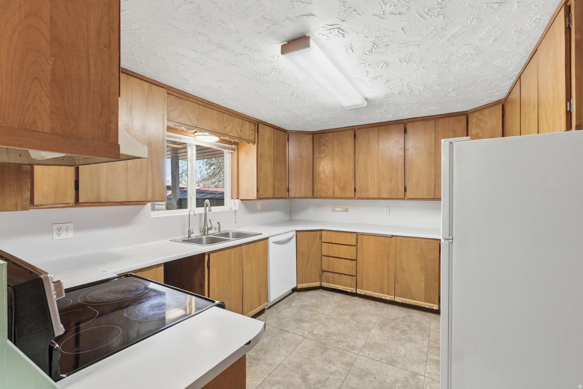 Kitchen featuring white appliances, light countertops, wood finish cabinets, a textured ceiling, and light tile patterned floors