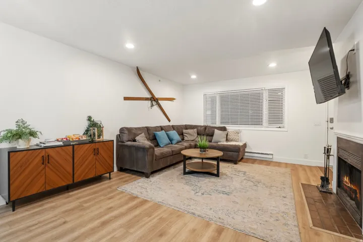 Living room with a lit fireplace, light wood-type flooring, a baseboard heating unit, and recessed lighting