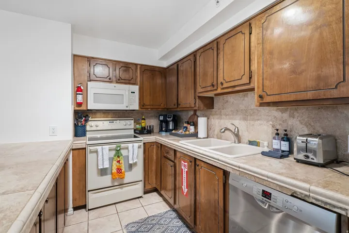 Kitchen featuring white appliances, tasteful backsplash, light tile patterned floors, and wood finish cabinetry