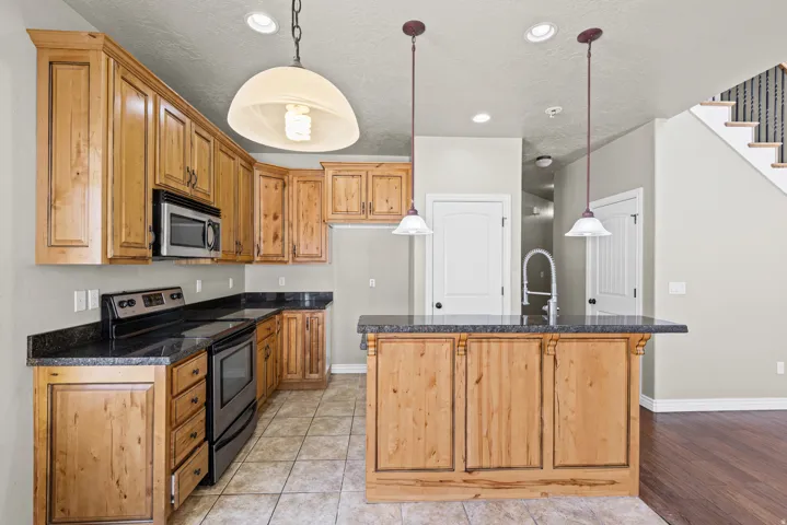 Open-concept kitchen featuring wood cabinetry, dark countertops, tile flooring, stainless steel appliances, and a central island with pendant lighting