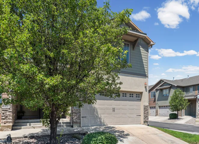 Contemporary townhome exterior featuring a two-car garage, stone accents, and a mature front yard tree