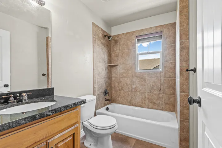 Bathroom featuring a tiled shower/tub combination, single vanity with dark countertop, wood-finish cabinetry, and neutral wall paint