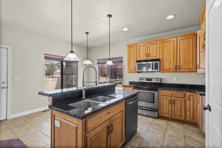 Kitchen featuring a dual basin sink with a gooseneck faucet, an island with countertop seating, stainless steel appliances, wood cabinetry, and tiled flooring