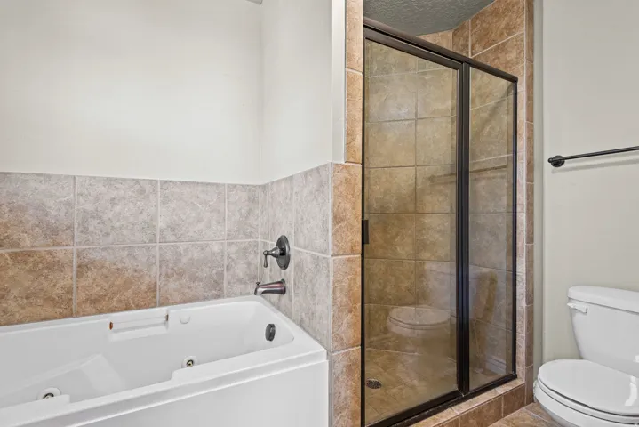 Bathroom featuring a white soaking tub with dark-toned fixtures, a framed glass shower enclosure, and neutral-toned wall and floor tiling