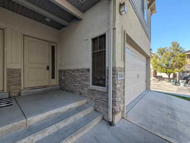 Entrance to property featuring stone siding, stucco siding, concrete driveway, and an attached garage