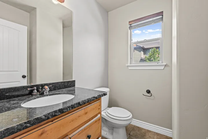 Bathroom featuring a wood-finish vanity with a dark speckled countertop, an undermount oval sink, and bronze-finish fixtures