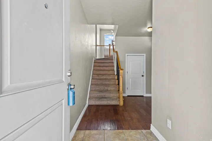 Entryway featuring a tiled floor transition to wood-finish flooring, a carpeted staircase with wood handrails and metal balusters, and a white paneled door