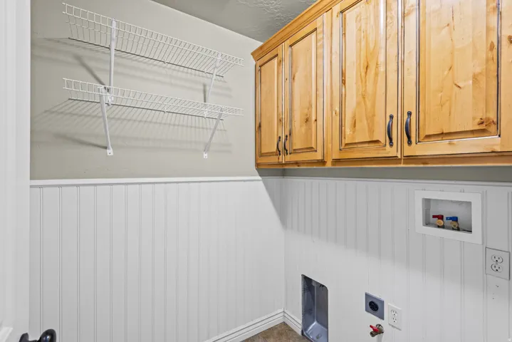 Utility area featuring natural wood cabinetry with dark hardware, white beadboard wainscoting, and wall-mounted wire shelving