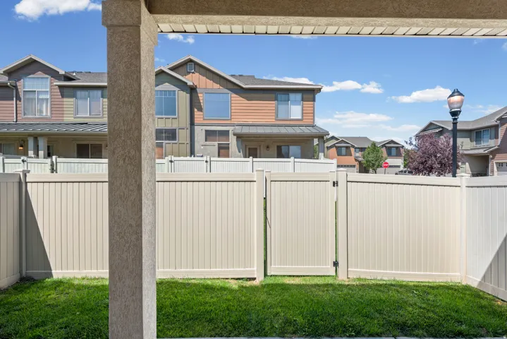 Enclosed backyard featuring a manicured lawn and tan vinyl fencing with a gate