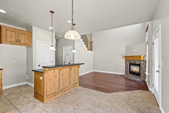 Open-concept kitchen and living area featuring a custom wood-finish island with black countertop and pendant lighting, ceramic tile flooring, stainless steel appliances, white cabinetry, and a gas fireplace with surround