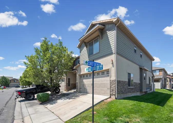 Contemporary townhome exterior featuring dual-tone siding, a stone veneer base, an attached two-car garage, and a concrete driveway
