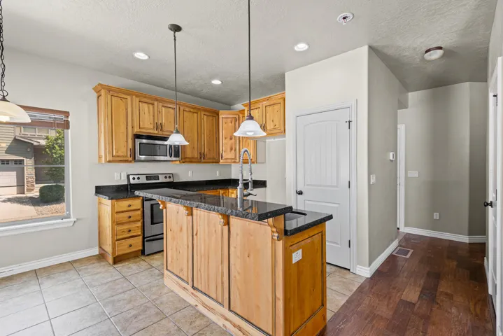 Kitchen featuring wood cabinetry, stainless steel appliances, dark stone countertops, and a central island with pendant lighting