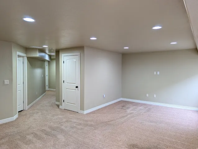 Recessed lighting illuminates neutral-toned walls and plush carpeting, featuring white trim and solid doors