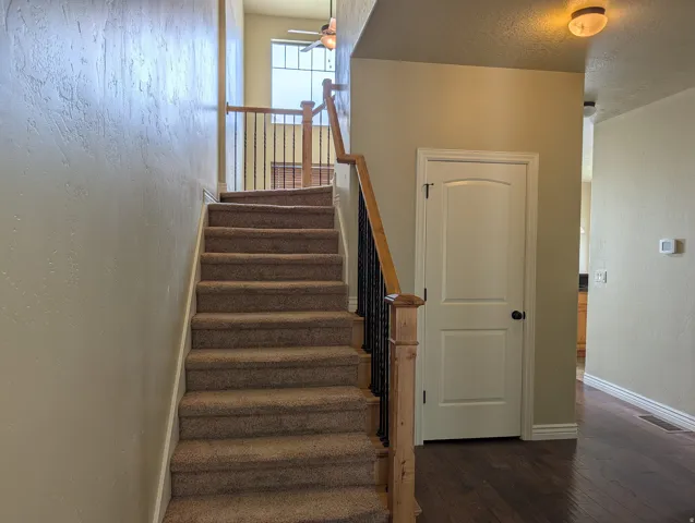 Carpeted staircase with wood newel posts and wrought iron balusters