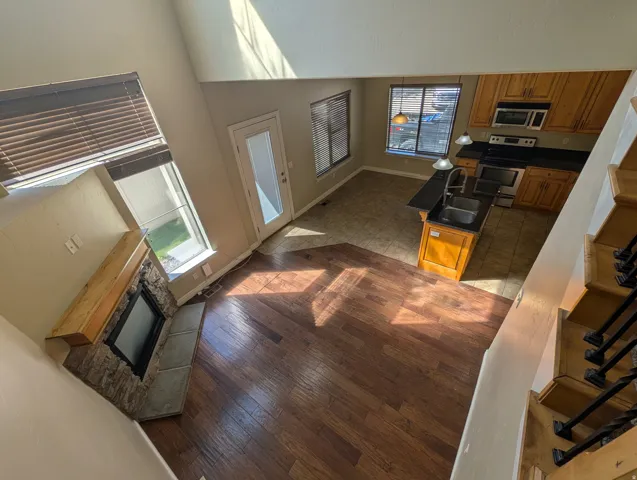 Kitchen with wood finish cabinets, dark countertops, stainless steel range with electric stovetop, a high ceiling, and an island with sink