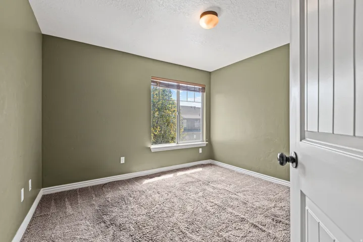 Carpeted room with a window featuring wood blinds and a view of exterior buildings and trees
