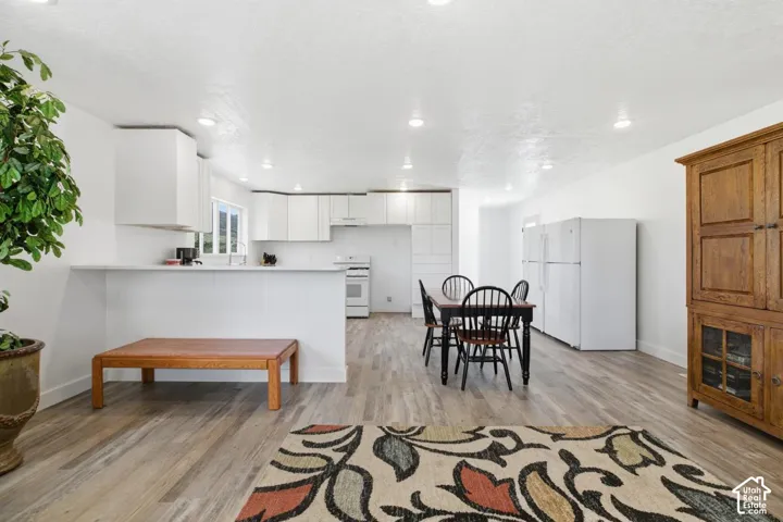 Kitchen with white appliances, a peninsula, light countertops, light wood-style floors, and white cabinets