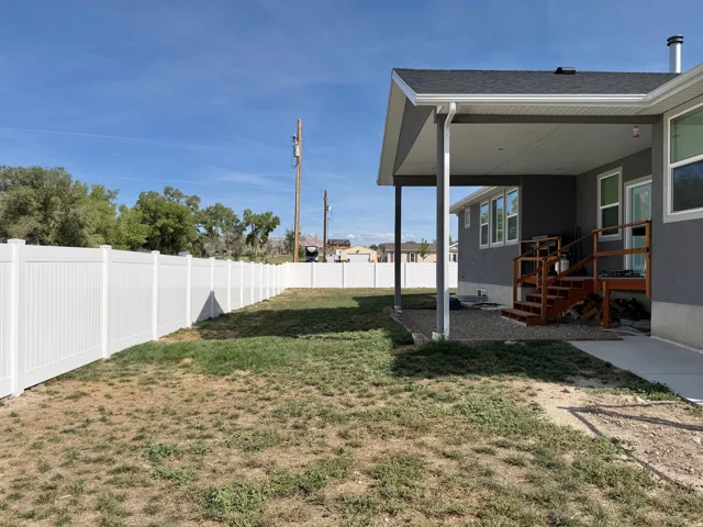 Expansive backyard featuring a white privacy fence, covered patio, and wood stairs with railing