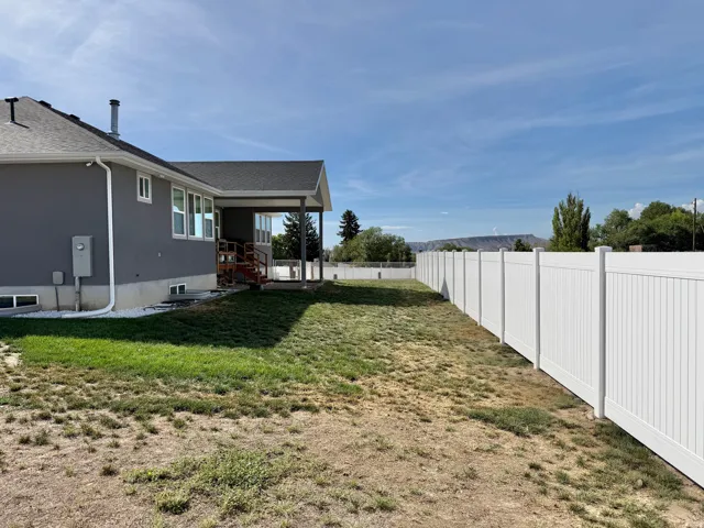 Expansive backyard featuring a white vinyl privacy fence, a covered patio with a grey roof, and a low-maintenance stucco exterior