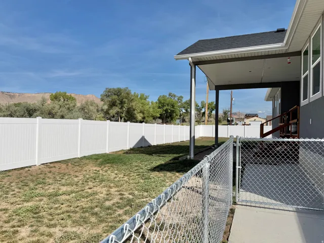 Expansive backyard featuring a white vinyl privacy fence, chain link fencing, a covered patio, and a concrete walkway