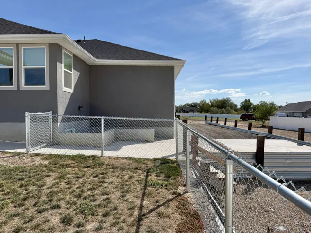 Exterior featuring gray stucco siding, multiple windows, a chain link fence, and a concrete patio