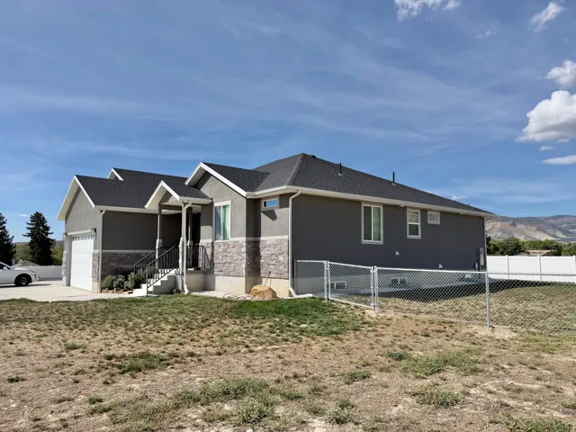Contemporary exterior featuring stucco and stone veneer, a covered entry, an attached garage, and a chain-link fence