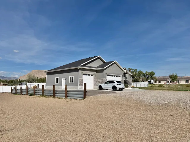 Contemporary residence with a stucco and stone veneer exterior, multiple garage doors, and a gravel driveway