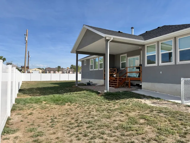 Expansive backyard featuring a white vinyl fence, covered patio, wood deck, and multiple windows
