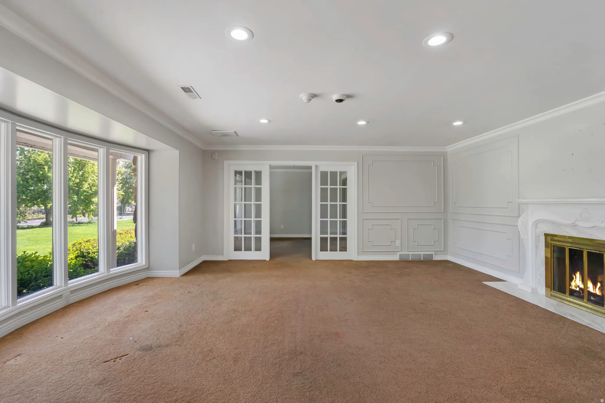 Unfurnished living room featuring crown molding, recessed lighting, a high end fireplace, carpet floors, and french doors