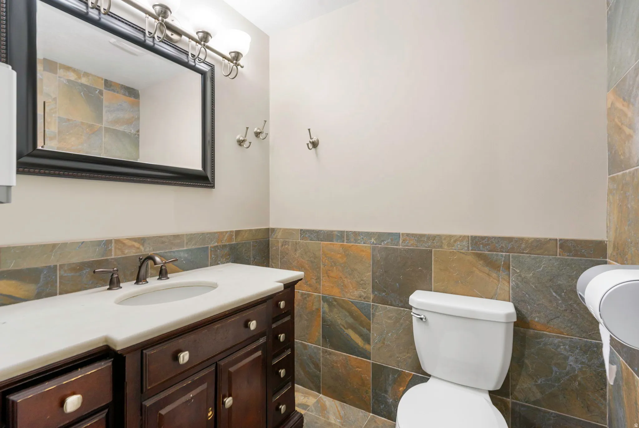 Half bathroom featuring vanity, tile walls, and wainscoting