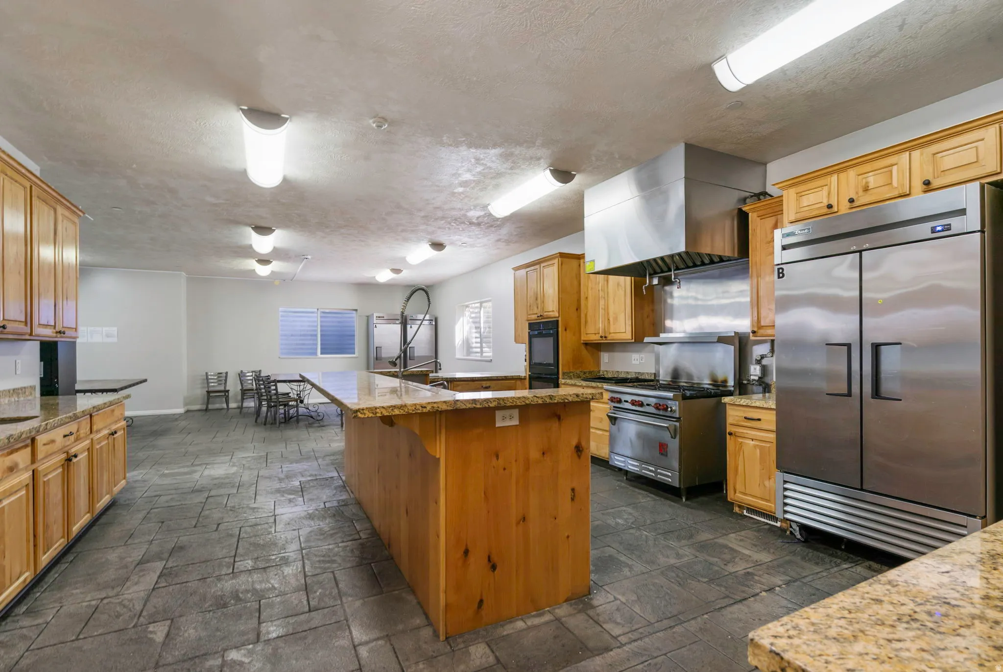 Kitchen with high end appliances, stone tile flooring, a textured ceiling, a center island, and light stone counters