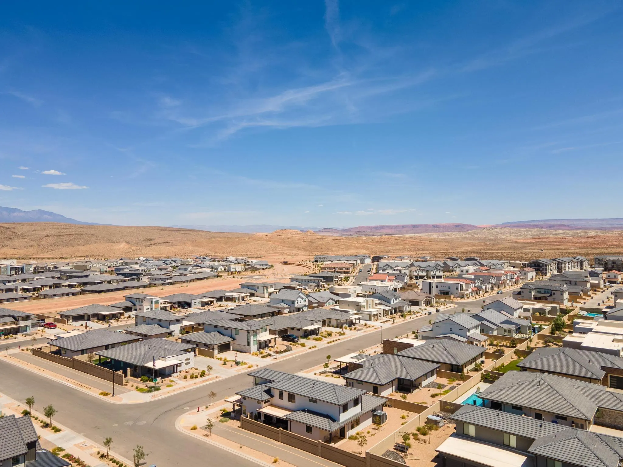 Expansive residential development featuring contemporary architecture with numerous homes, asphalt roads, and desert landscaping