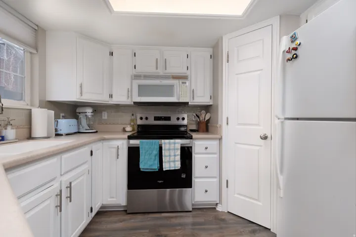 Kitchen with white appliances, white cabinets, light countertops, and dark wood finished floors