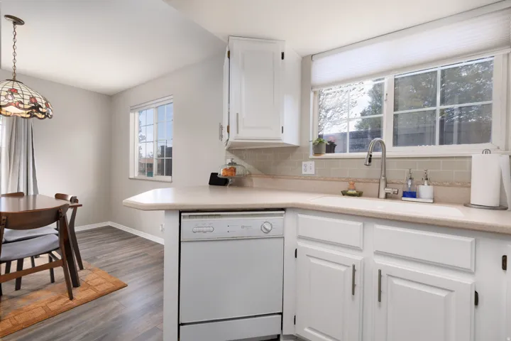 Kitchen with light countertops, white cabinetry, white dishwasher, and tasteful backsplash