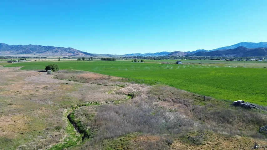Expansive agricultural land featuring varied terrain, a winding stream, and distant mountain ranges