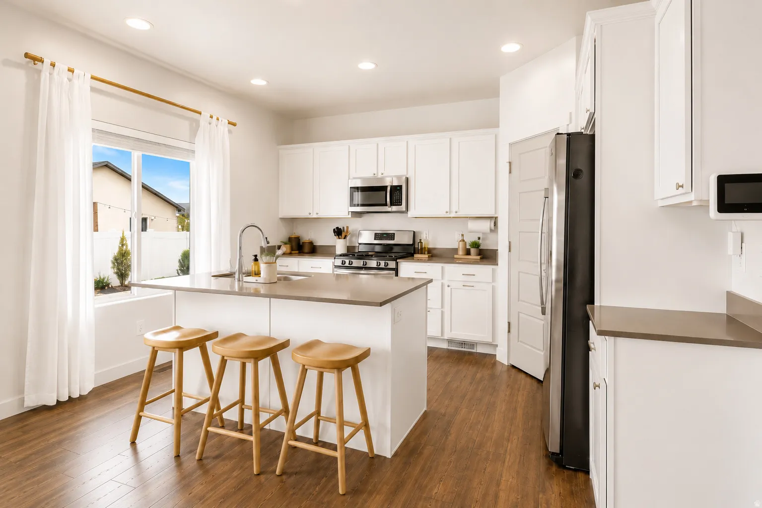 Kitchen featuring a central island with an integrated sink, white cabinetry, stainless steel appliances, wood-finish flooring, and recessed lighting