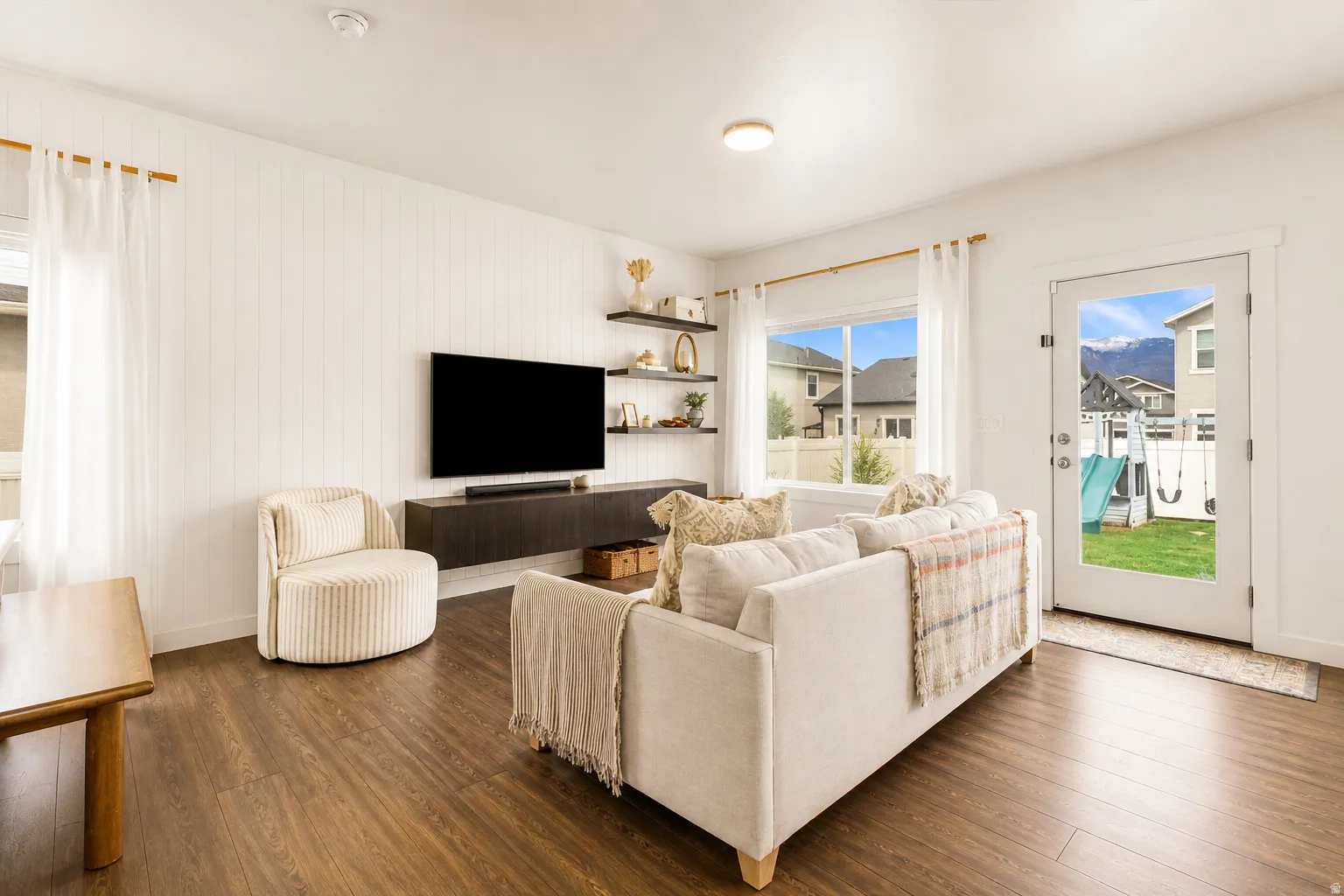 Living area featuring wood-finish flooring, white shiplap accent wall, and a built-in media console with shelving