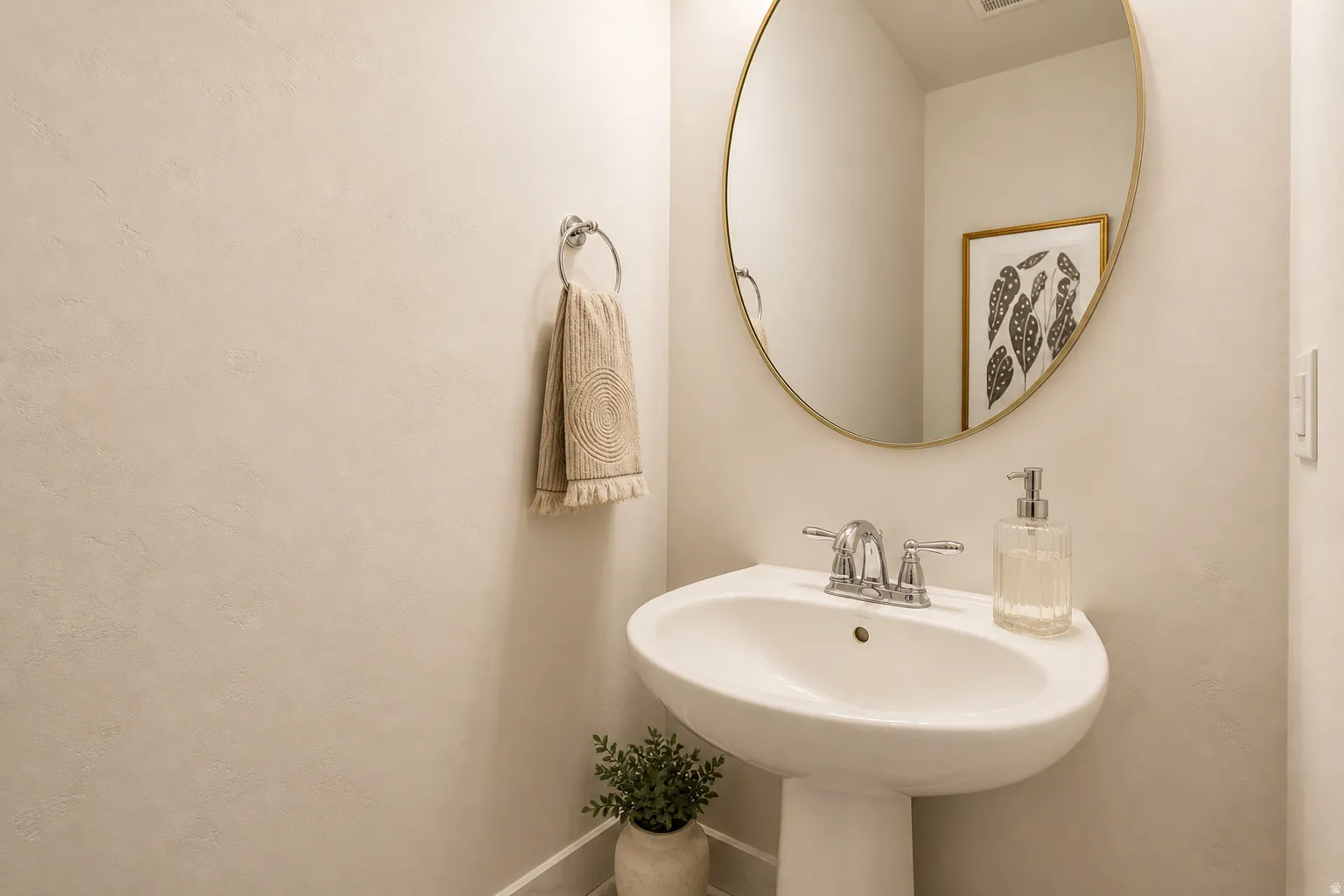 Pedestal sink with chrome faucet, complemented by an oval-framed wall mirror