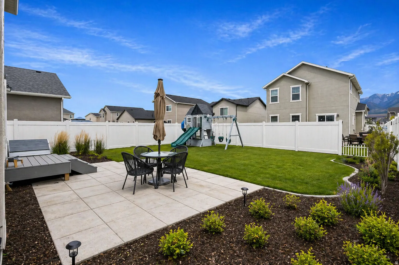 Fenced backyard featuring a patio area, a playground, outdoor dining area, and a residential view