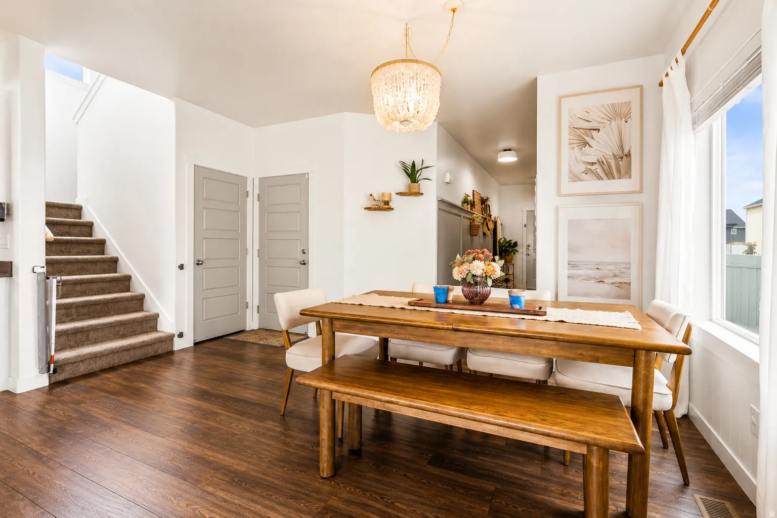 Dining area with wood-finish flooring, a large window with sheer curtains, and a beaded chandelier