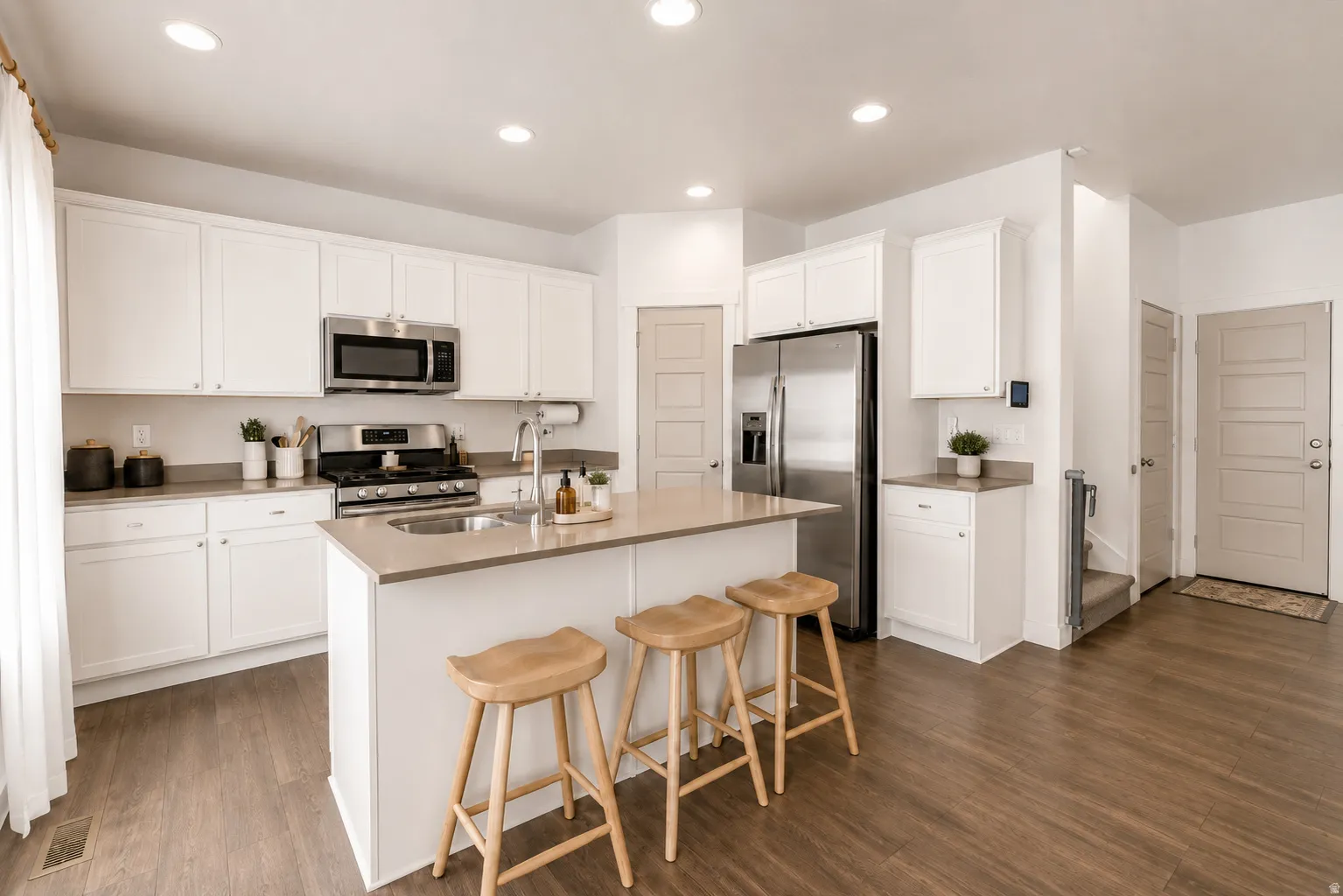 Kitchen featuring an island with a built-in sink, stainless steel appliances, recessed lighting, white cabinetry, and wood-finish flooring