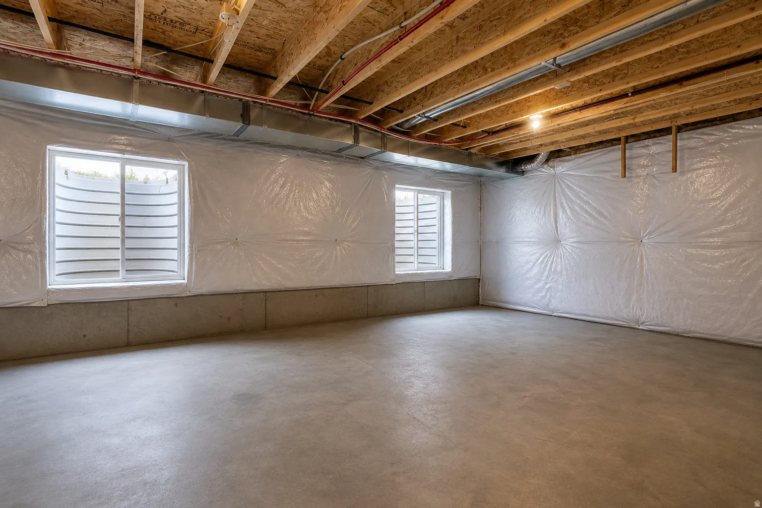 Unfinished basement space featuring exposed wood joists, concrete flooring, two egress windows, and insulated walls