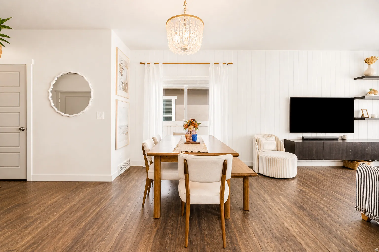 Open-concept living space featuring wood-finish flooring, a contemporary chandelier, and shiplap accent wall