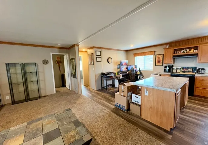Kitchen featuring light countertops, black range with electric cooktop, crown molding, a center island, and dark carpet